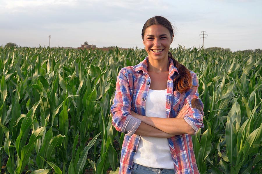 Business Insurance - Farmer Standing In Her Corn Field With Her Arms Crossed Looking Proud
