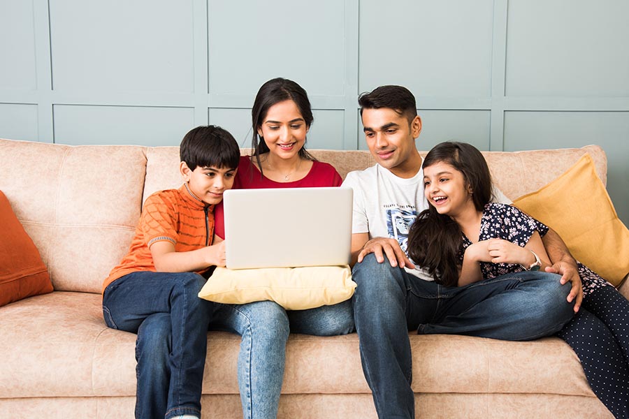 Client Center - Family Sitting Close on a Couch Using a Laptop, Parents With Their Arms Around the Pre-Teen Children
