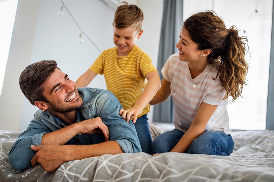 Personal Insurance - Father, Mother and Son Laughing and Playing Together on a Bed